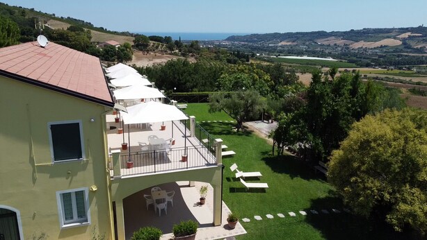 A two-story building with a balcony, outdoor seating, and a view of the countryside. - AGRITURISMO MONTEMAGGIO (Lapedona)