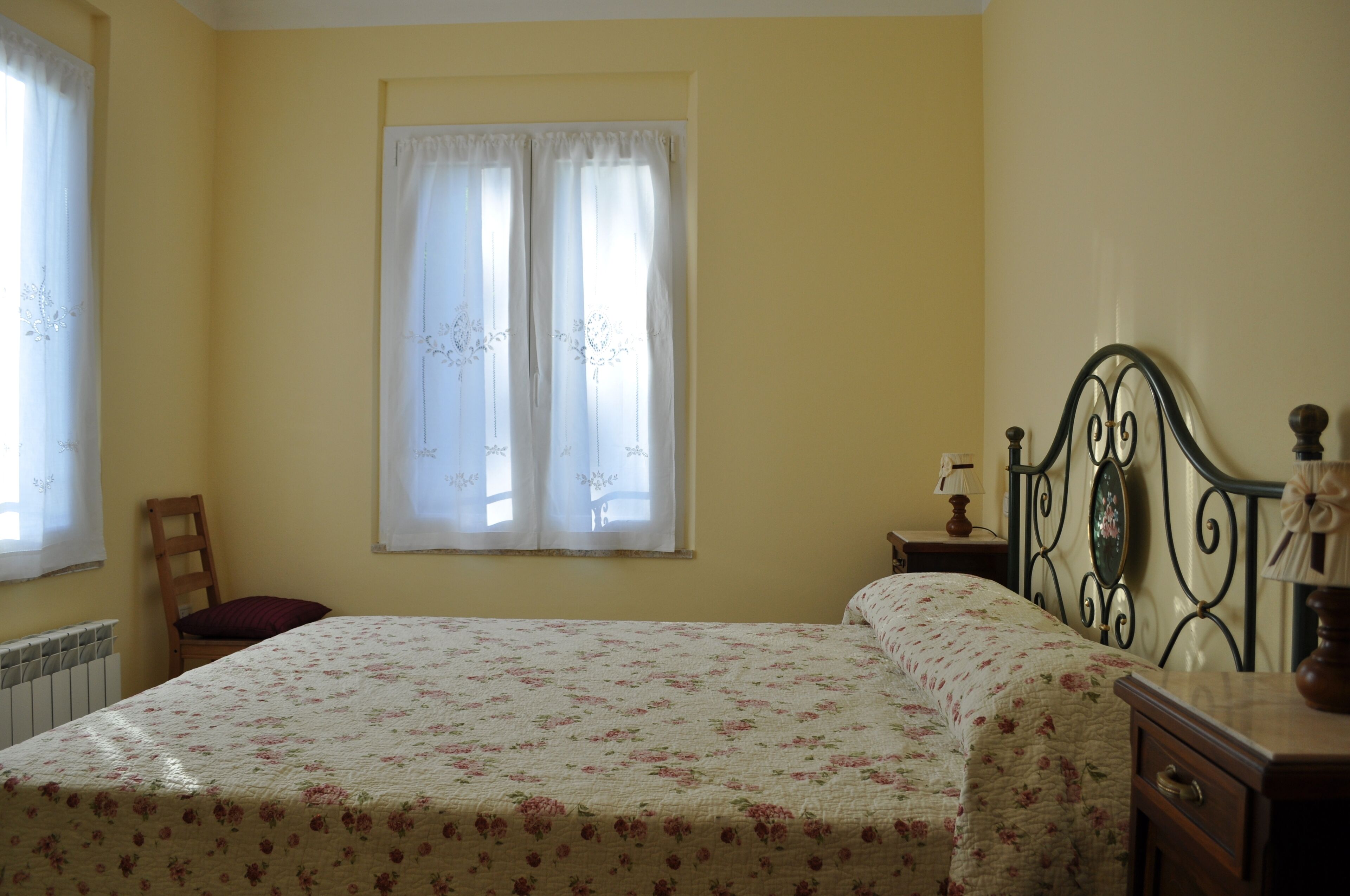 Une chambre à coucher avec un lit, une chaise, une table de chevet et une fenêtre avec des rideaux.