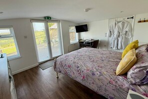 A bedroom with a bed, a desk, a TV, and a wardrobe. - 1 Bed Cabin-sleeps 2, Hot Tub, Garden, Pets, Views (Callington)