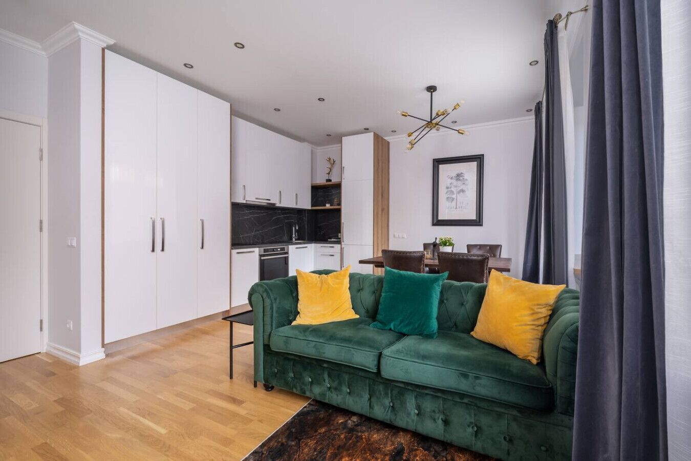 A modern living room with a green sofa, yellow and green cushions, a wooden coffee table, and a dark curtain.