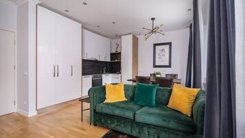 A modern living room with a green sofa, yellow and green cushions, a wooden coffee table, and a dark curtain.