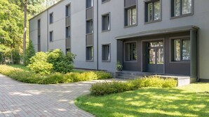 Ein modernes Gebäude mit flachem Dach, zahlreichen Fenstern und einem gepflasterten Weg, der zu einer Rasenfläche mit Büschen führt.