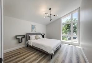 A bedroom with a bed, a modern chandelier, a large window, and a unique wall art piece.
