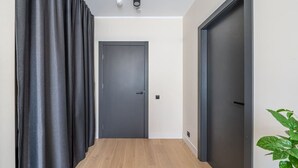 A hallway with a wooden floor, a dark door at the end, and a plant on the right. - Beach and forest front apartment in Dzintari (Jūrmala)