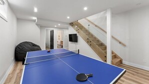 A ping pong table in a room with a staircase and a bean bag chair. - THE FRISKY BEAVER - Spacious, modern cottage in Grand Bend (Lambton Shores)