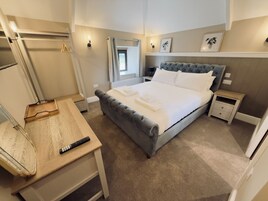 Un dormitorio con cama, mesitas de noche, un escritorio y un espejo.