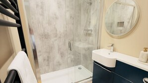A modern bathroom with a glass shower enclosure, a white toilet, a sink with a dark cabinet, and a round mirror on the wall. - Rising Sun Inn - Bronn Ewhella (Launceston)