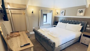A bedroom with a large bed, a bedside table, a desk with a chair, a mirror, and a window with curtains. - Rising Sun Inn - Bronn Ewhella (Launceston)