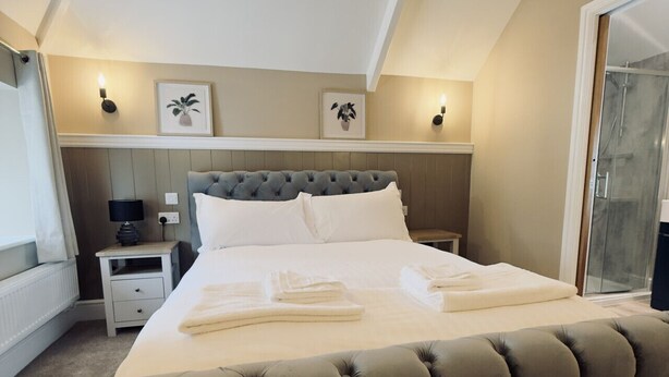 A bedroom with a large bed, a bedside table, a nightstand, and a glass shower door. - Rising Sun Inn - Bronn Ewhella (Launceston)