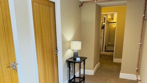 A hallway with carpeted floors, wooden doors, and a table with a lamp.