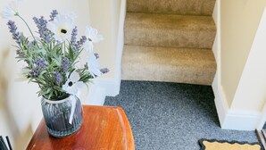A wooden console table with a vase of flowers, a doormat with "welcome" written on it, and a carpeted staircase.