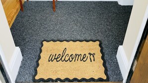 A carpeted entrance with a welcome mat and a small table with a vase of flowers.