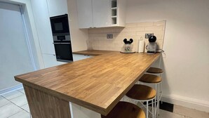 Eine Küche mit einer Holzausziehtheke, weißen Schränken, einem eingebauten Backofen und einer Kaffeemaschine.