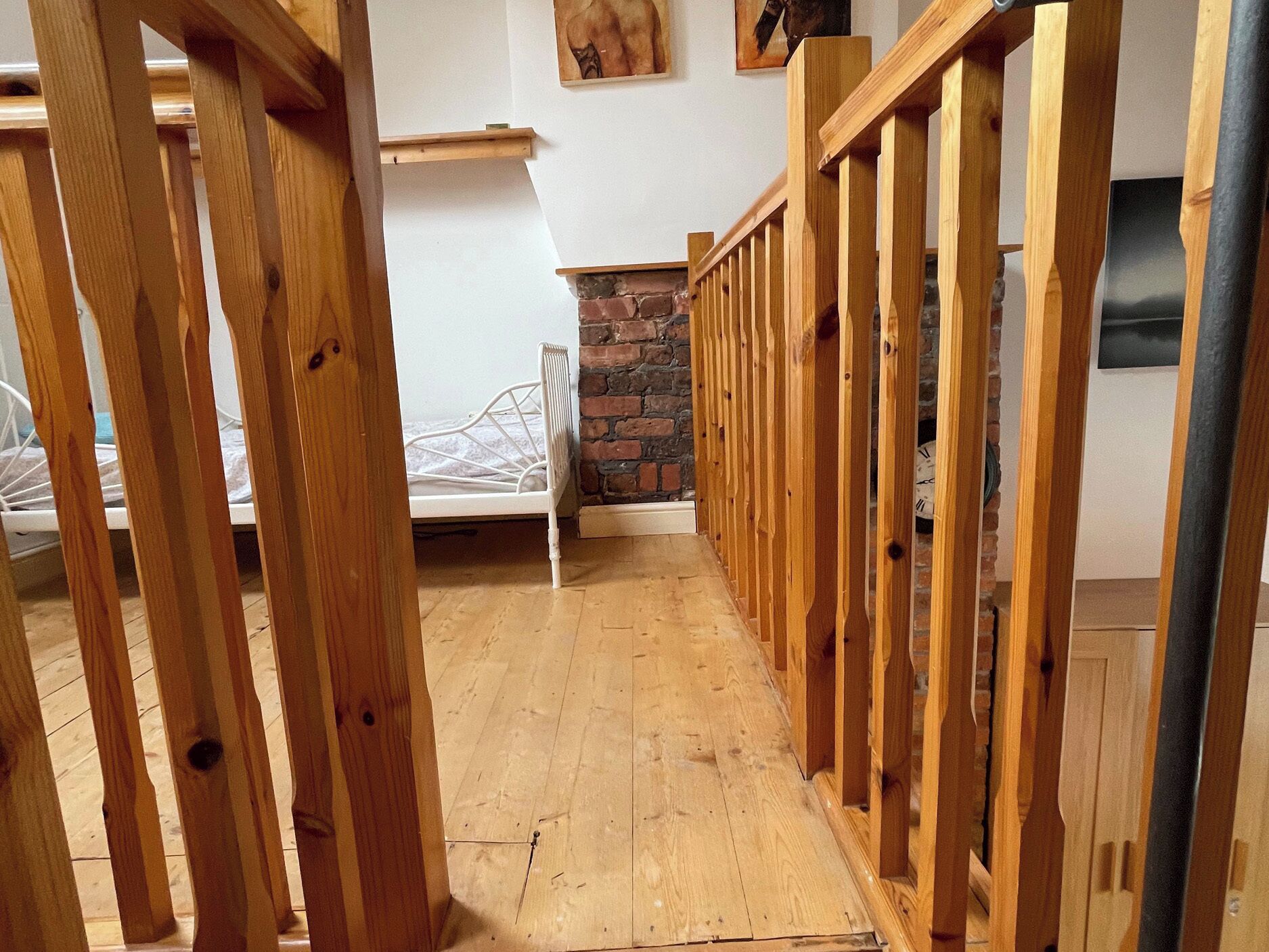 A narrow wooden staircase leading to a bedroom with a white metal bed frame and a brick fireplace.