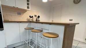 Eine Küche mit weißen Schränken, einer Holz Arbeitsplatte und drei weißen Hocker.