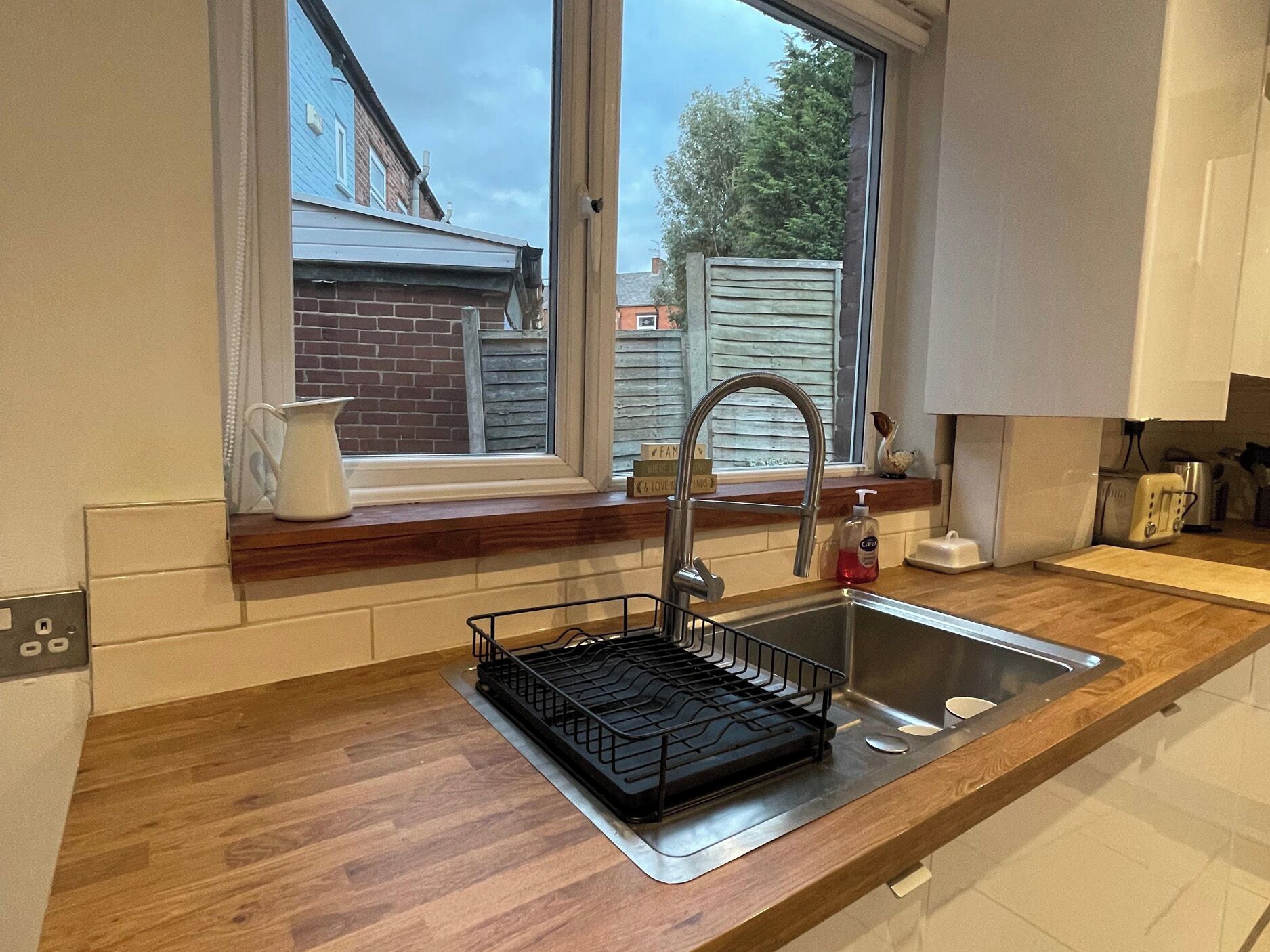A modern kitchen with a stainless steel sink, a dish rack, and a window overlooking a residential area.