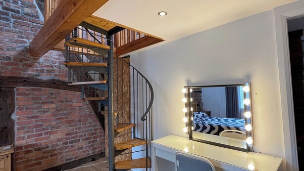 Ein Zimmer mit Wendeltreppe, Schminktisch mit Spiegel und Beleuchtung sowie einer Backsteinwand.
