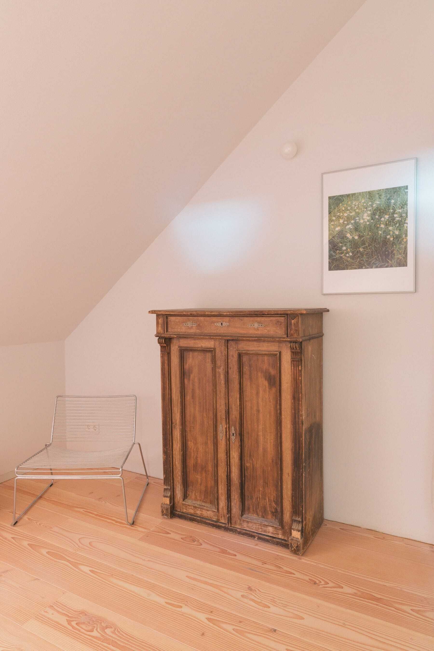 Une pièce avec un meuble en bois, une chaise en métal et un tableau encadré accroché au mur.