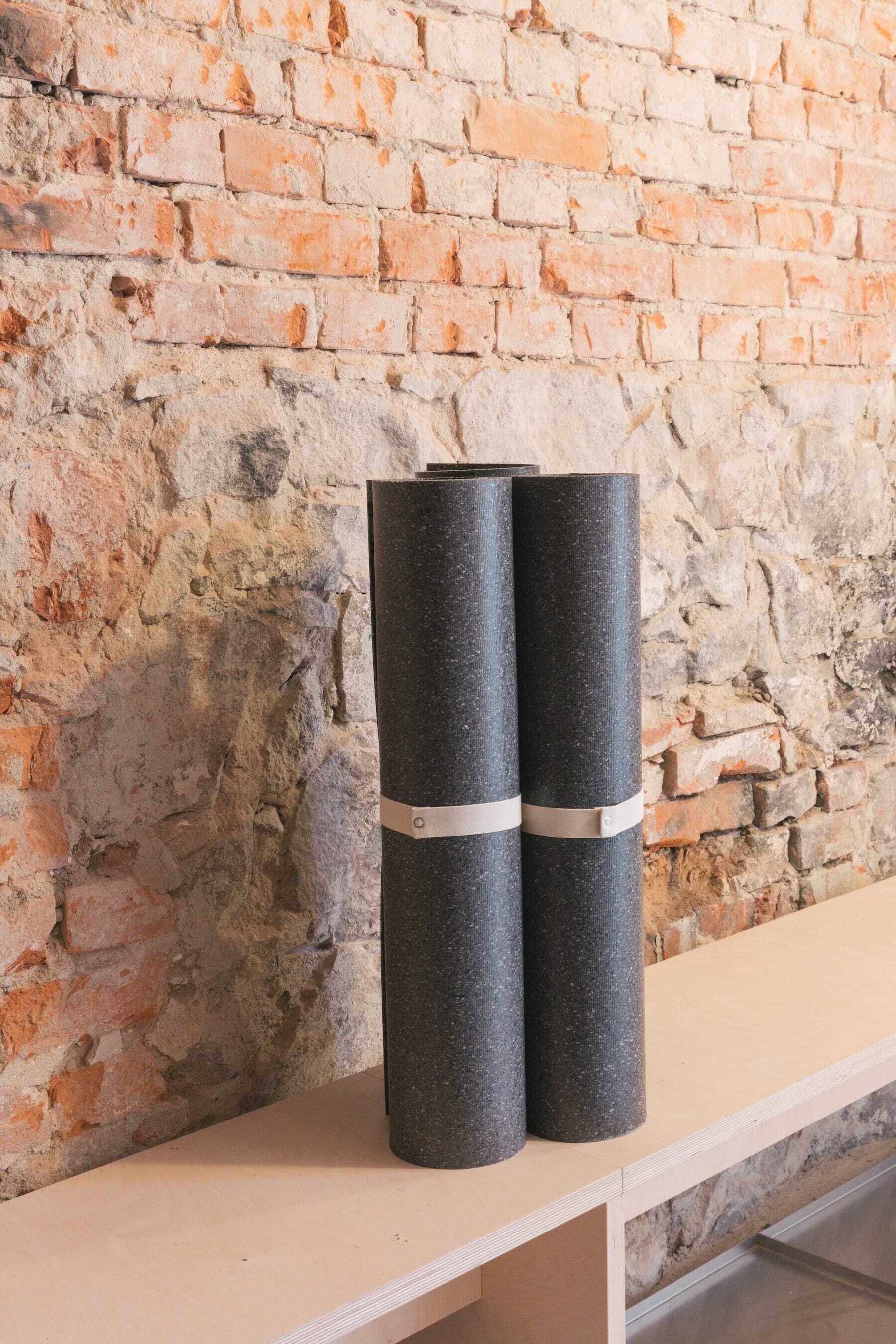 Deux objets cylindriques, cerclés de métal, sont posés sur une étagère, adossée à un mur de briques.