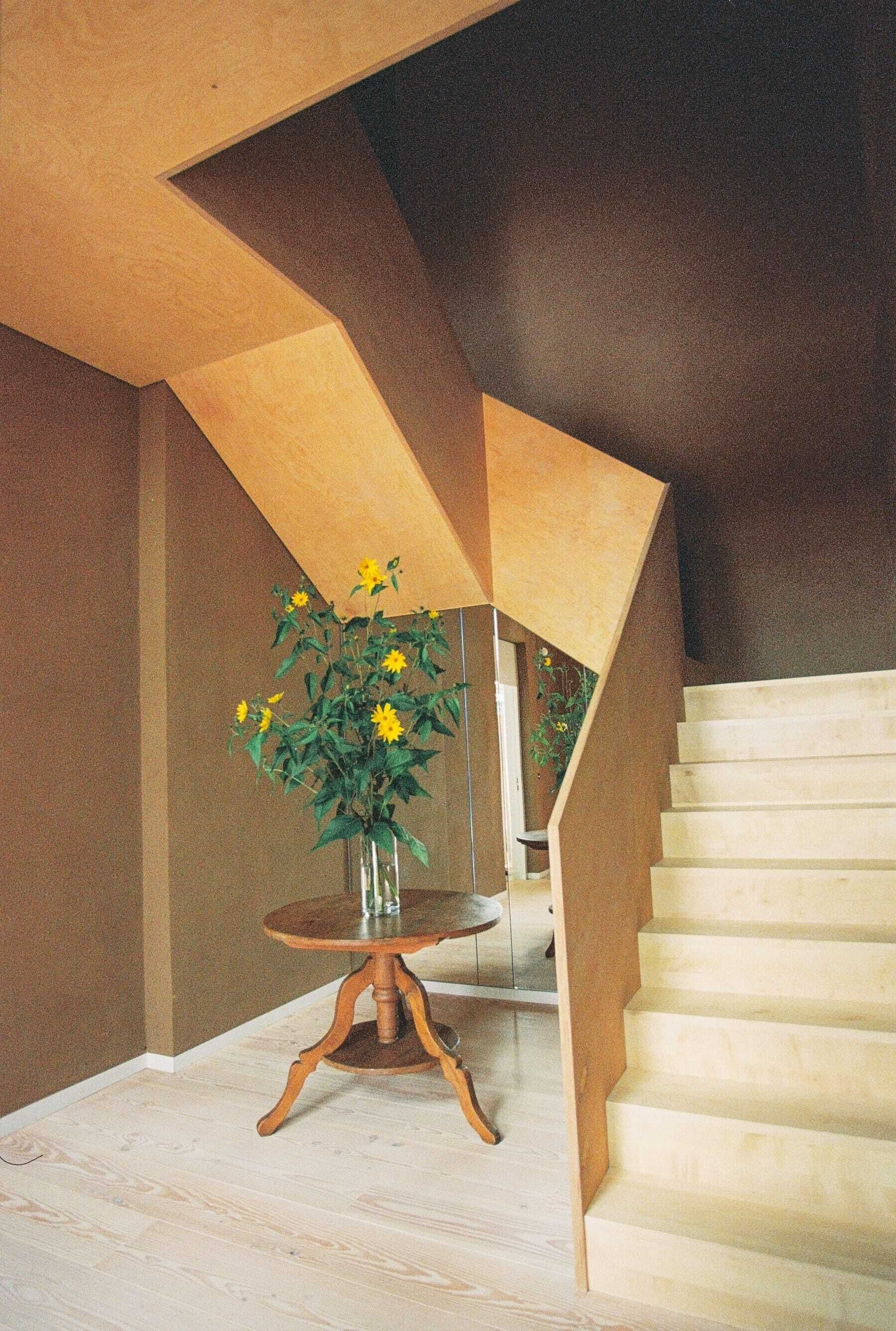 Un escalier avec des éléments en bois et un vase rempli de fleurs jaunes, posé sur une petite table.