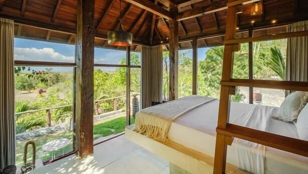 A room with a bed, large windows, and a view of greenery. - Ocean Bay Retreat (Pecatu)