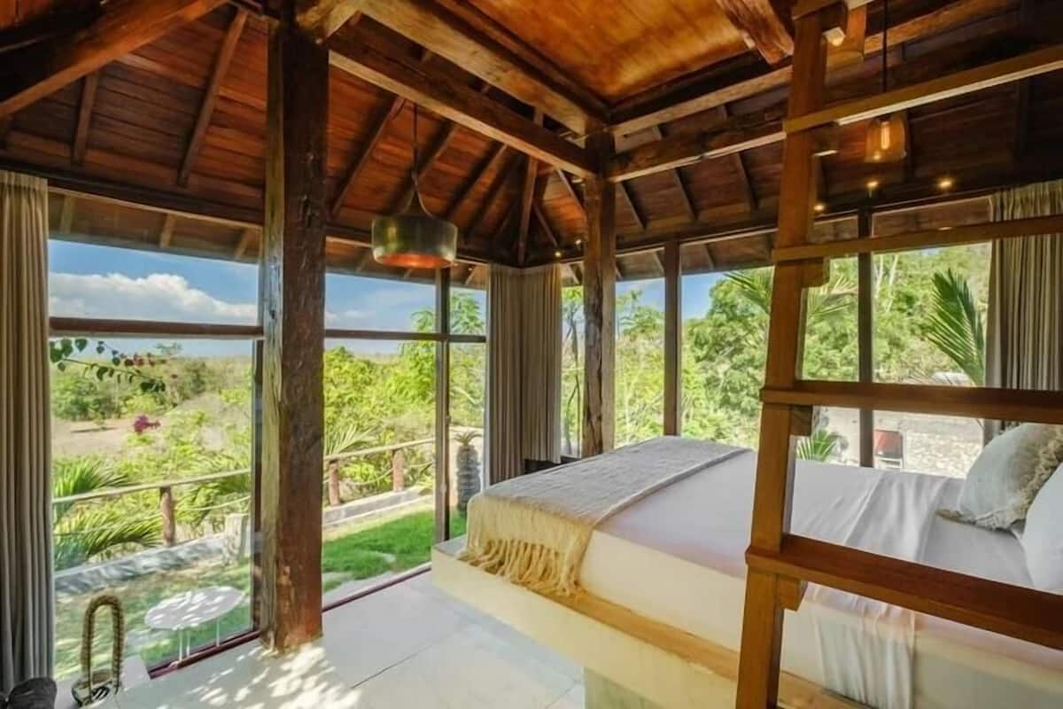 A room with a bed, large windows, and a view of greenery.