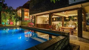 A swimming pool with a stone deck, a bar area with a wooden counter, and a dining area with a bench and table. - Ocean Bay Retreat (Pecatu)