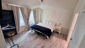 Un dormitorio con cama, mesitas de noche, un perchero y una ventana con cortinas.