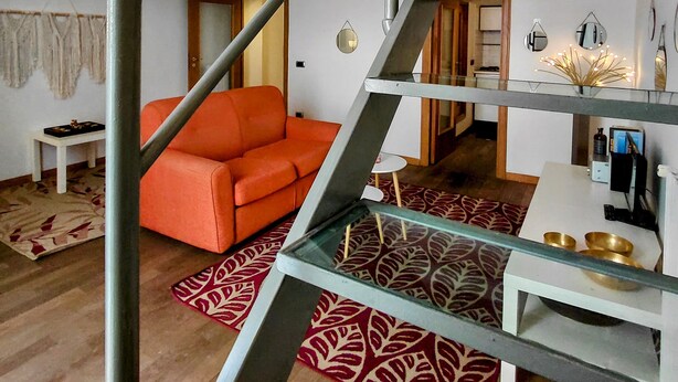 Een modern interieur met een trap, een bank, een eetgedeelte met een glazen tafel, en een keuken in de achtergrond.