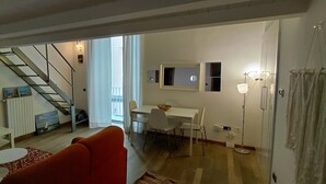 Een woonkamer met een bank, een televisie, een eethoek met een tafel en stoelen, een trap en uitzicht op de omgeving.