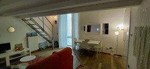 Un salon comprenant un canapĂ©, un tĂ©lĂ©viseur, un coin repas avec une table et des chaises, un escalier et une vue sur lâextĂ©rieur.