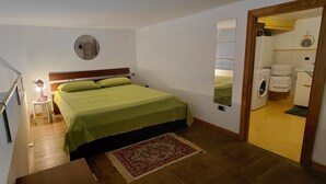 Een slaapkamer met een bed, een spiegel, een nachtkastje, een dressoir, en een zichtbare badkamer door een open deur.