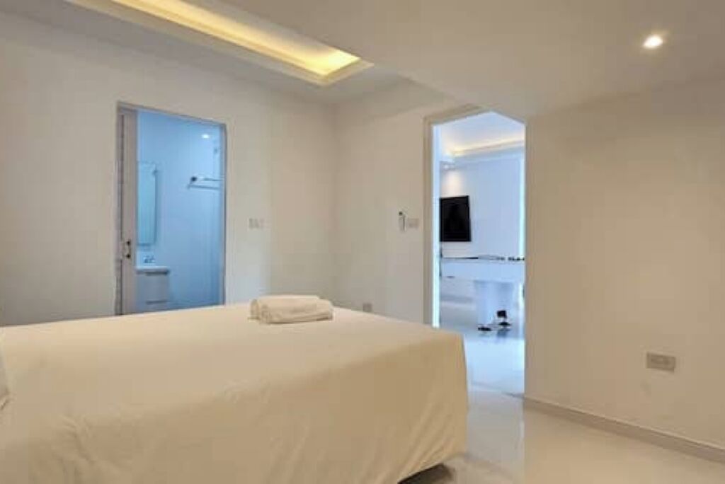 Una habitación de hotel moderna con una cama grande, una puerta que da a un baño y un televisor montado en la pared.