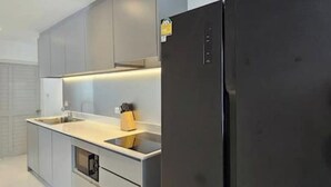 Une cuisine moderne avec des meubles gris, un réfrigérateur noir et un évier en acier inoxydable.