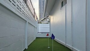 A narrow corridor with artificial green flooring, white walls, and a white fence on one side.
