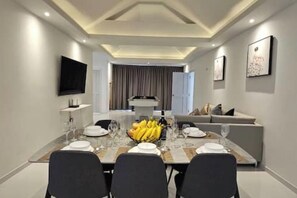A dining area with a long table set for four, a television mounted on the wall, and a modern ceiling design. - Villa 129 Wongamat, 4 Beds. (Pattaya City)