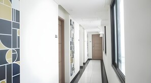 A corridor with a modern design, featuring a number of doors and a large window on the right. - Bianco Costel (Central Bogor)