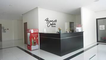 Una recepción con un refrigerador de Coca-Cola, un letrero en la pared que dice 'Bianco Castel Bogota' y una puerta de vidrio a la derecha.