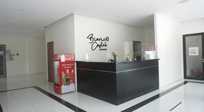 A reception desk with a Coca-Cola refrigerator, a wall sign reading 'Bianco Castel Bogota', and a glass door to the right. - Bianco Costel (Central Bogor)