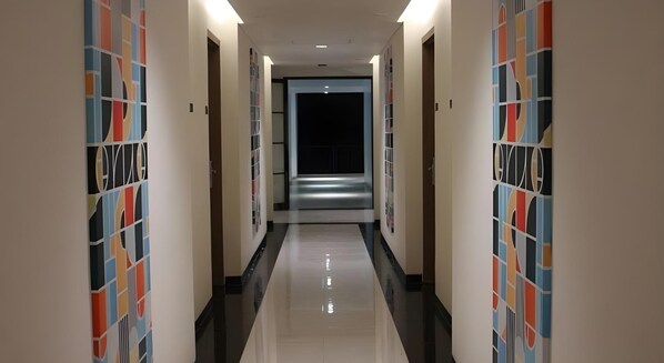 A corridor with a reflective floor and patterned walls, leading to a darkened room. - Bianco Costel (Central Bogor)