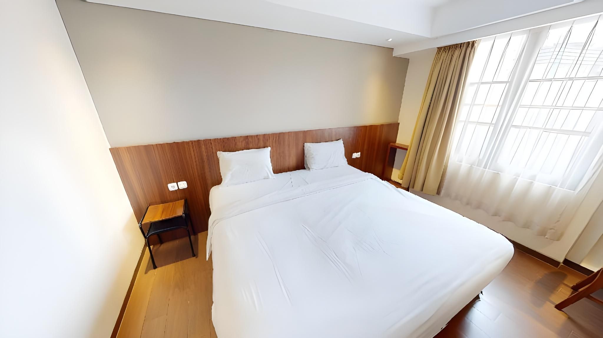 Una habitación de hotel con una cama grande, cabecero de madera, mesitas de noche y una ventana con cortinas.