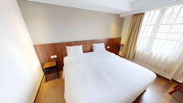 Una habitación de hotel con una cama grande, cabecero de madera, mesitas de noche y una ventana con cortinas.