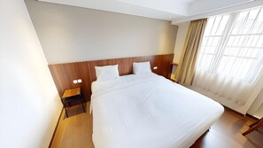 A hotel room with a large bed, wooden headboard, bedside tables, and a window with curtains. - Bianco Costel (Central Bogor)