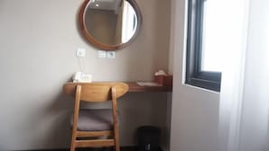 A room with a wooden chair, a round mirror, a small table, a window, and a trash bin. - Bianco Costel (Central Bogor)