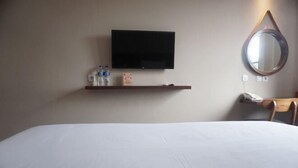 A hotel room with a bed, a mounted TV, a shelf with toiletries, a bedside telephone, and a mirror. - Bianco Costel (Central Bogor)