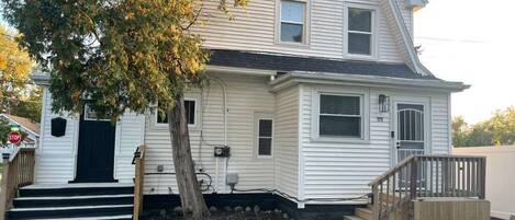 A two-story house with a front porch, a tree, and a wooden deck.