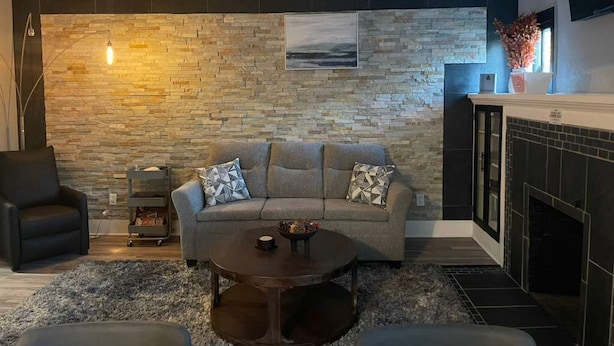 A living room with a stone wall, a sofa, a coffee table, and a fireplace. - 4 Bed Cozy Home closely located near downtown (Lansing)