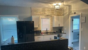 A modern kitchen with a black island, white cabinets, and a brick accent wall. - 4 Bed Cozy Home closely located near downtown (Lansing)