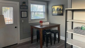 A dining area with a table and two black barstools, a window with blinds, a framed certificate on the wall, and a shelf with storage boxes. - 4 Bed Cozy Home closely located near downtown (Lansing)