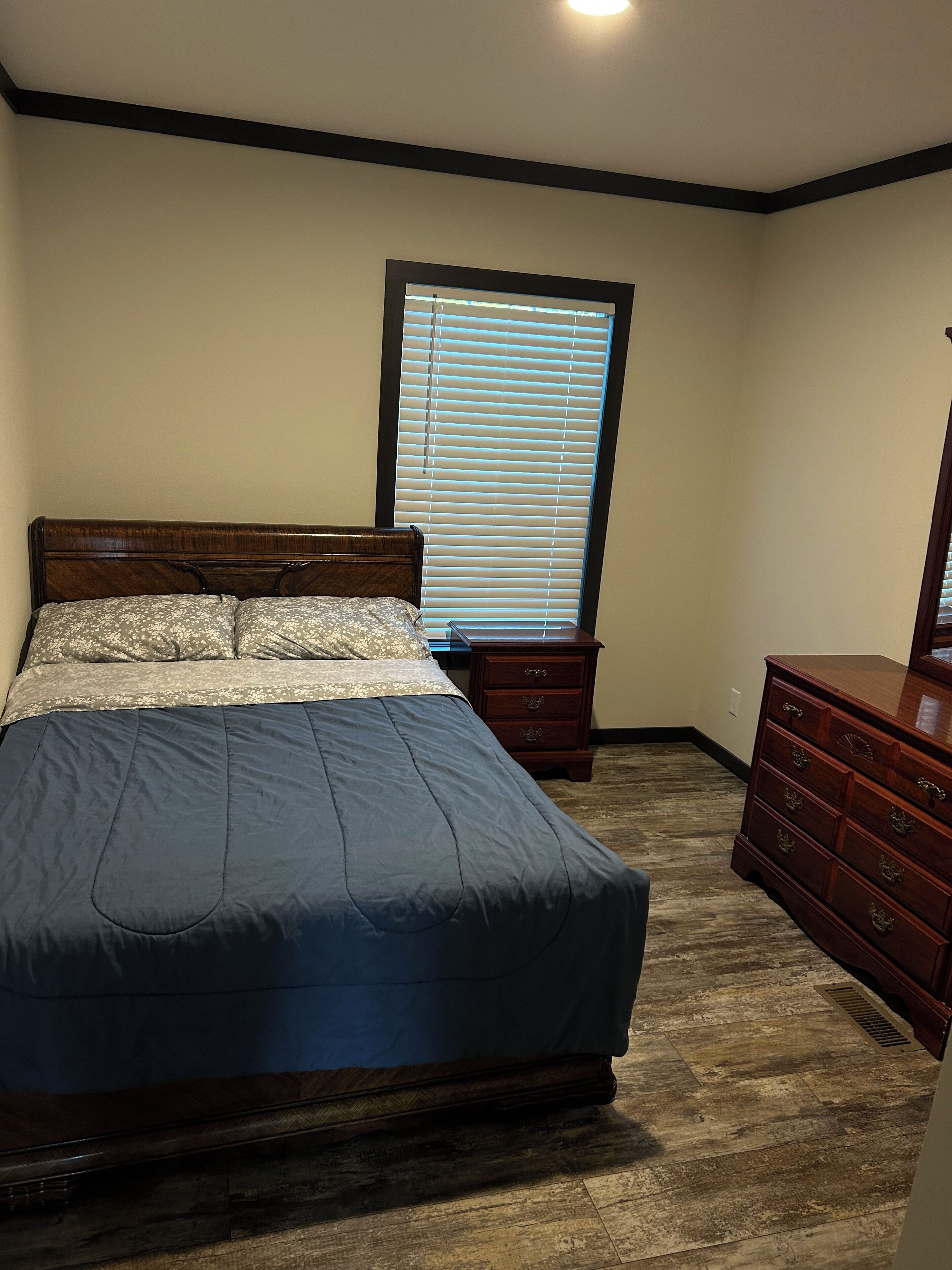 A bedroom with a bed, a dresser, a nightstand, and a window with blinds.